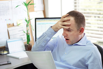 Obraz premium Office worker man reading negative news in letter. Shocked businessman. Business manager received layoff message letter from company feeling surprised. An agitated male without joy.