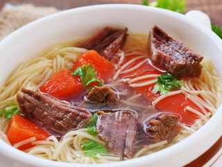 Beef soup with noodles and vegetables in soup bowl closeup