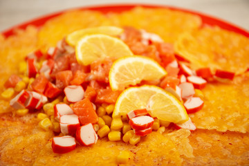 a delicious salad with salmon, corn, crab sticks, cheese and lemon slices lies on a red plate