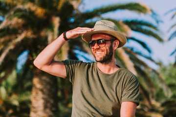 Young man standing by the palm trees looking at sun