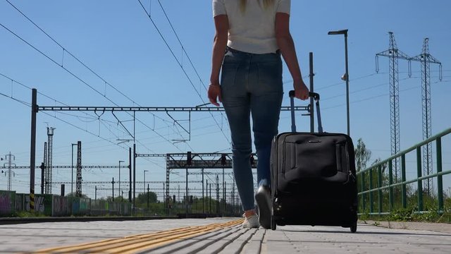 A woman with a suitcase walks along a deserted train station platform - view from the ground