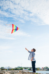 happy caucasian little kid playing with flying kite near sea shore at summer sunset