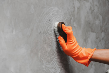 Hand of man wearing orange rubber gloves is used to convert scrub cleaning on the concrete wall.