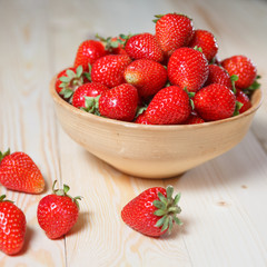 Fresh strawberries in a bowl on wooden table with low key scene.
