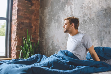 handsome young man waking up in his bed during morning time at home
