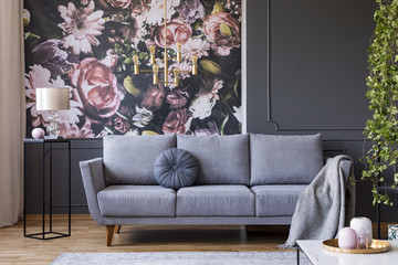 Real photo of dark living room interior with glass lamp, floral wallpaper, molding on wall and sofa...