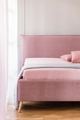 Fototapeta na wymiar Powder pink double bed with light blue blanket standing in real photo of bright bedroom interior