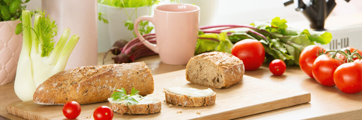 Close-up of bread on a cutting board with tomatoes and other vegetables around on a wooden kitchen table