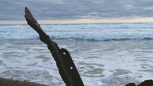 Rough surf in the background of a rusty piece of debris of a stranded ship wreck on the beach