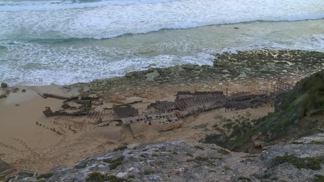 Wide shot with left to right pan from high point of view over the skeleton a stranded ship wreck on the beach