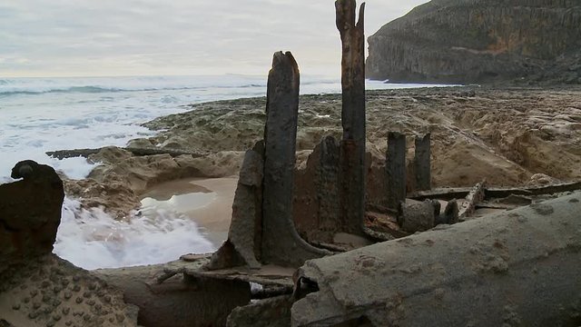 Close up of a ship wreck&rsquo;s rusty debris on a rocky beach, surrounded by calm waves