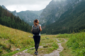 Rear shot of young brunette backpacker woman hiking on the green pathway in Tatra Mountains to Rysy...