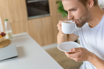 selective focus of young man drinking coffee at kitchen