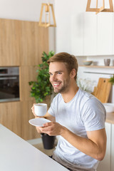 Fototapeta na wymiar happy young man drinking coffee on breakfast at kitchen table