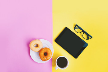 Cup of coffee, donuts, eyeglasses and tablet on pastel background with copy space