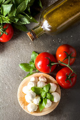 Balls of mozzarella with basil leaves, tomato and olive oil on rustic background