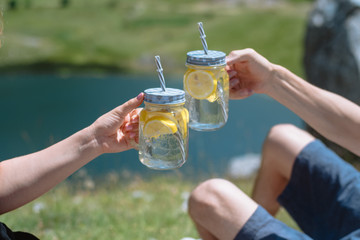 Two hands with lemonade on picnic against mountains with lake on background. Montenegro