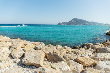 Beautiful landscape of turquoise clear blue sea with rocks and breakwater and mountains in the background