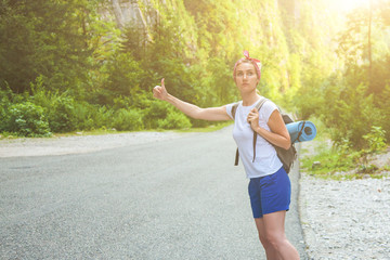 Beautiful girl traveler hitchhiking in the mountains