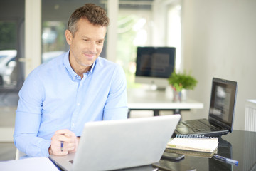 Fototapeta premium Successful in business life. Middle aged businessman with laptop in the office