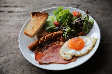 English breakfast  fried egg, ham,sausage, bacon,salad and toast on wood background in mystic light