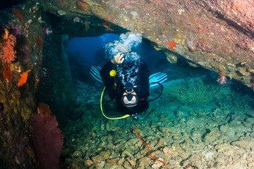 SCUBA diver swimming upside down through an underwater swimthrough on a tropical coral reef