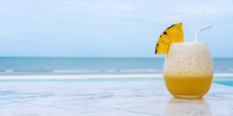 Pineapple smoothie on marble table with blue tropical beach. Summer holiday concept.