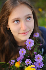 Fototapeta premium Teen girl sits next to flowers that bloom violet flowers and dreamingly looks up