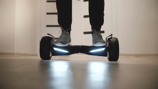 Close-up low angle shot of male legs in sneakers stepping on gyroscooter in apartment, riding backwards and walking away