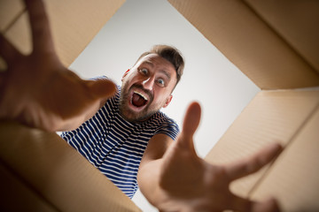 The surprised man unpacking, opening carton box and looking inside. The package, delivery,...
