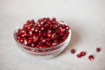 Red pomegranate seeds in glass bowl on gray background