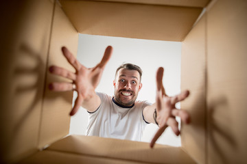 The surprised man unpacking, opening carton box and looking inside. The package, delivery,...