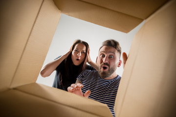 The surprised man and woman unpacking, opening carton box and looking inside. The package,...
