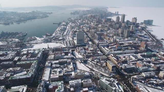 Aerial Top owerall urban cityscape Main square old Soviet new homes Waterfront Ships Port industry. Sea ocean coastal frozen white blue hills. Road traffic cars. Vladivostok Russia. Winter snow