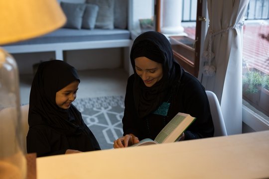 Mother assisting her daughter to read holy Quran at home