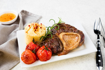 Prepared beef steak osso bucco with mashed potatoes and tomatoes on white table. Copy space