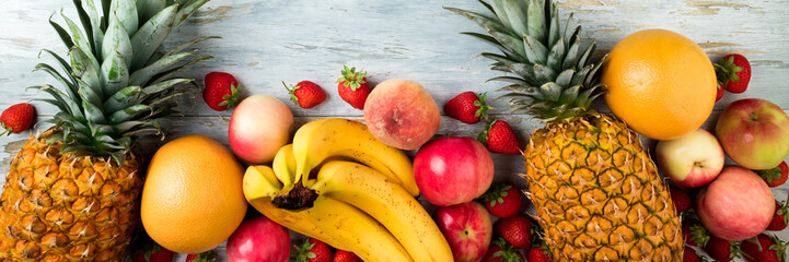 Variety of fruits on old wooden table. Pineapple, banana, apple, berry, citrus and peach. Healthy food clean eating selection. Top view. Copy space