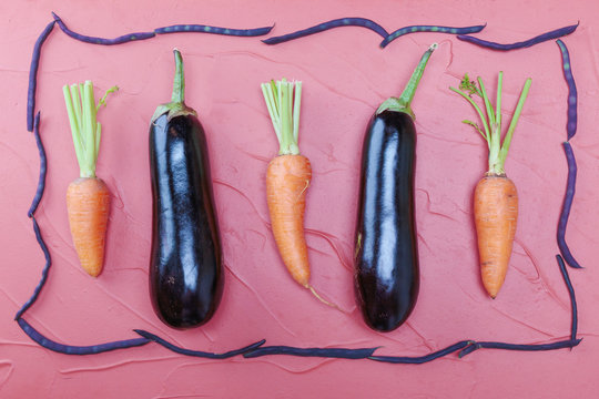Aubergines and carrots on a pink background in a frame of colored beans.