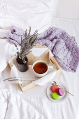 Morning breakfast in bed wooden tray with a cup of tea, sweet colorful french macaroons, love...