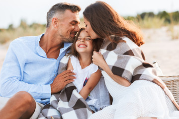 Parents hugging outdoors at the beach with their daughter.