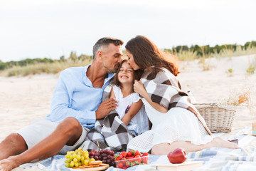 Parents hugging outdoors at the beach with their daughter.