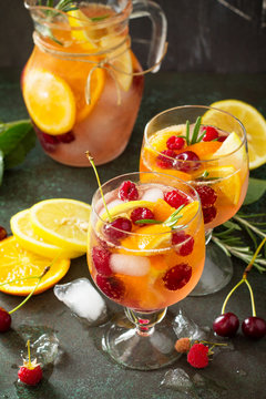 Homemade refreshing wine sangria or punch with fruits in glasses. Sangria cocktails with fresh fruits, berries and rosemary. On a stone or slate background, with a jug and ingredients.