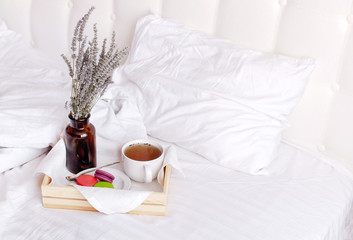 Fototapeta na wymiar Morning breakfast in bed wooden tray with a cup of tea, sweet colorful french macaroons, love letter, bouquet of lavender. Top view Morning at Hotel or at home. Background Concept Cozy morning