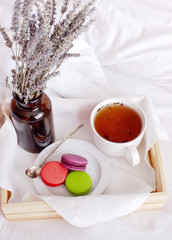 Morning breakfast in bed wooden tray with a cup of tea, sweet colorful french macaroons, love letter, bouquet of lavender. Top view Morning at Hotel or at home. Background Concept Cozy morning