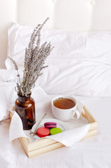 Morning breakfast in bed wooden tray with a cup of tea, sweet colorful french macaroons, love letter, bouquet of lavender. Top view Morning at Hotel or at home. Background Concept Cozy morning