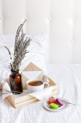 Morning breakfast in bed wooden tray with a cup of tea, sweet colorful french macaroons, love letter, bouquet of lavender. Top view Morning at Hotel or at home. Background Concept Cozy morning
