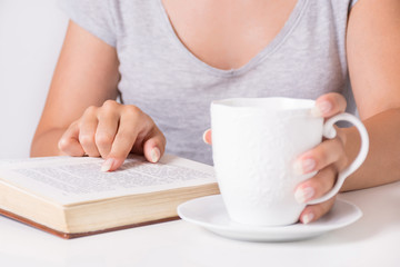 Young woman reading book and holding finger on text word. Girl relaxing with cup of coffee in hand. Education and beauty concept. Close up, selective focus