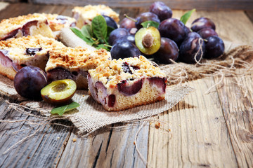 Rustic plum cake on wooden background with plums around.