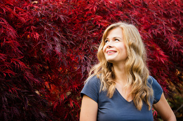 young woman portrait on a red maple tree leaves background. 