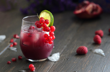 Glass of pomegranate juice with ice, decorated  with fresh red currant berries and lime  on rustic wooden table. Refreshing antioxidant drink for health.